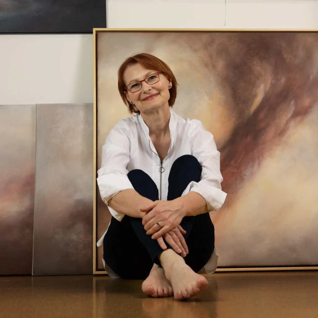 Malířka sedí před svými obrazy